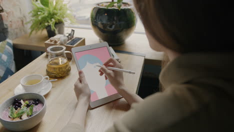 woman drawing a portrait on a tablet in a cafe