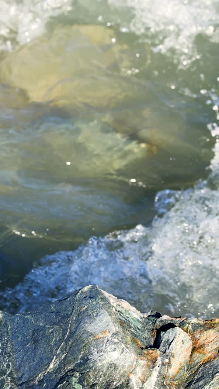 Onde dinamiche si infrangono contro le coste rocciose sotto la luce solare intensa, catturando la bellezza naturale e la potenza del Lago Wakatipu.