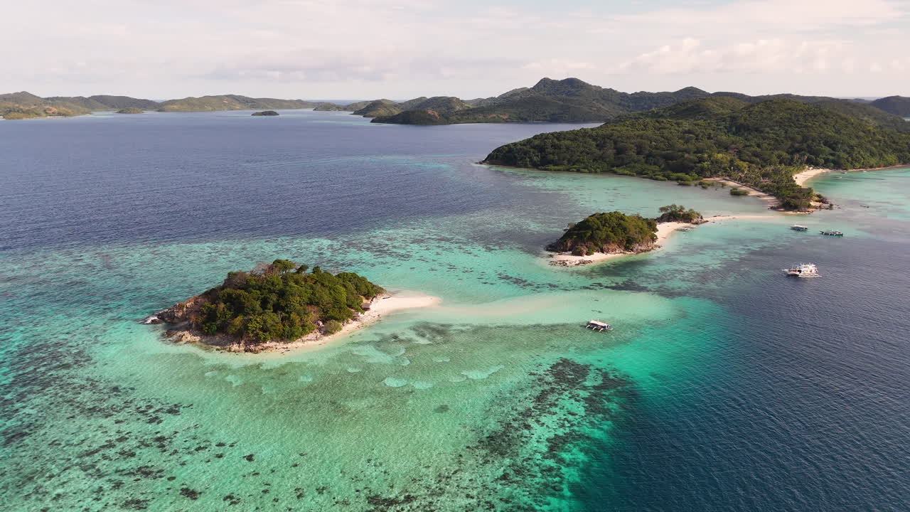 Aerial drone view of Coron Island’s dramatic cliffs, tropical greenery, and idyllic turquoise waters, Philippines. Wide rotating shot with small islands and shallow ocean water.
