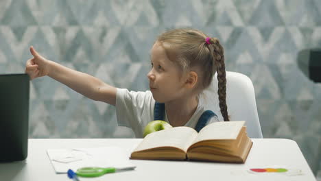 girl with plaits eats apple and shows thumb-up at table