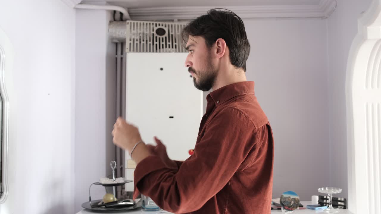 Attractive guy with a beard getting dressed and buttoning his shirt in front of a mirror,young man looking at his clothes