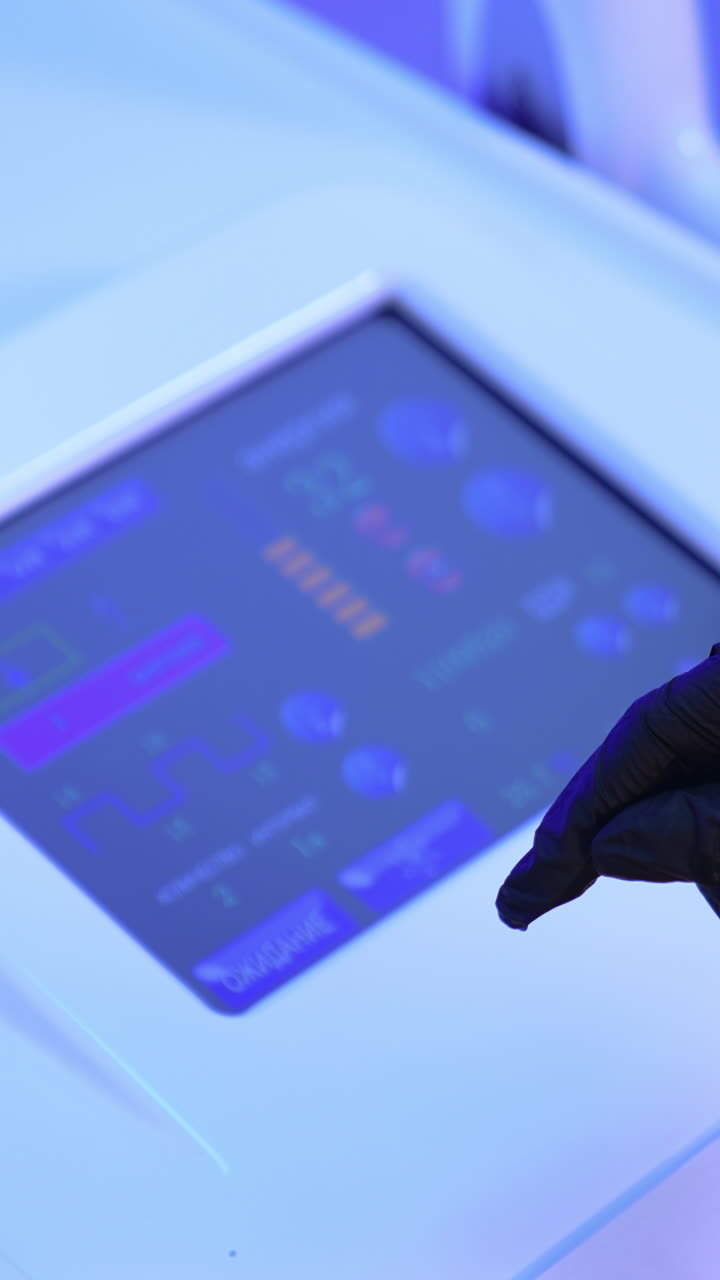 Gloved cosmetologist's hand chooses the necessary parameter on the sensor screen of equipment. Beautician prepares laser for usage. Vertical video