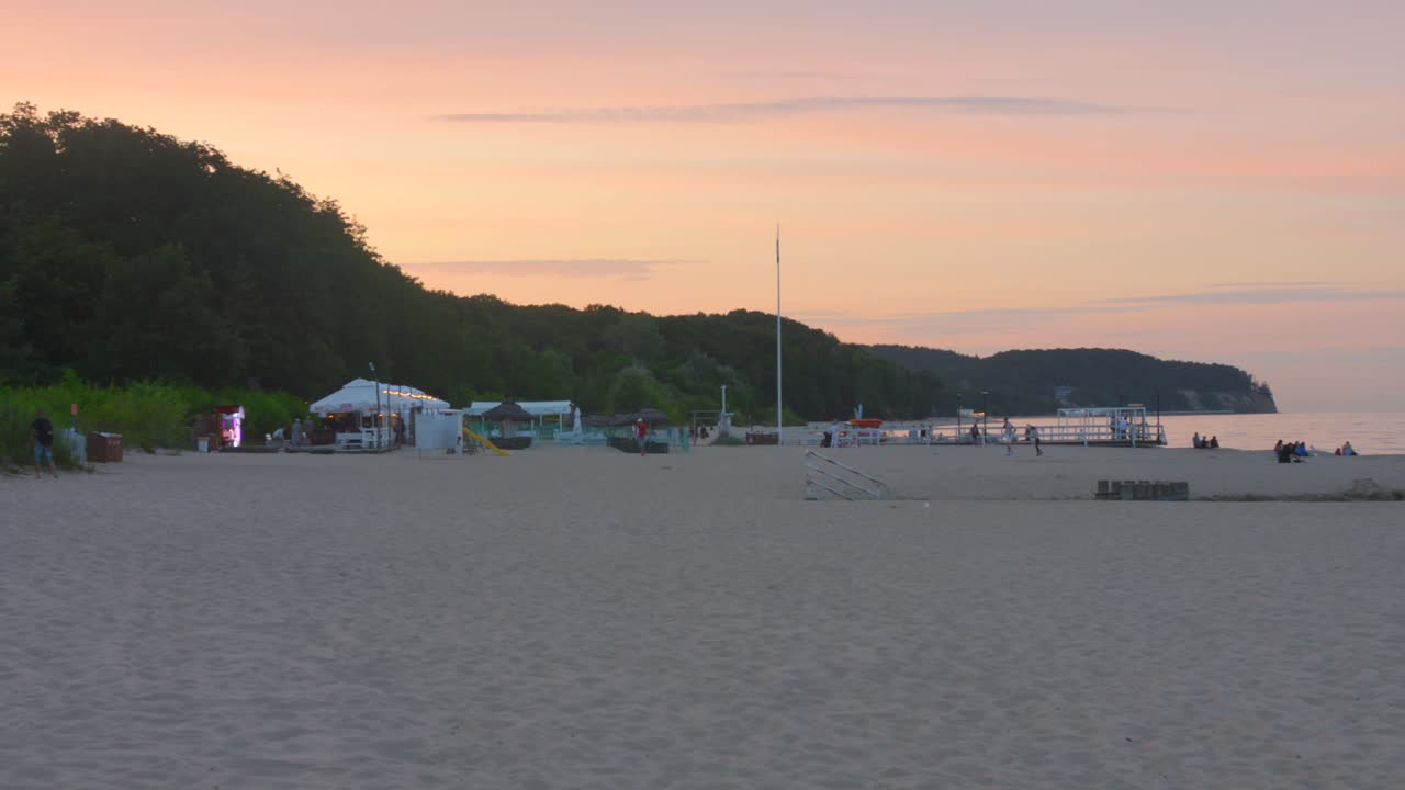 Sandy Shoreline With People Strolling At Sunset On The Northern Coast Of Poland Near Gdansk. Wide Shot