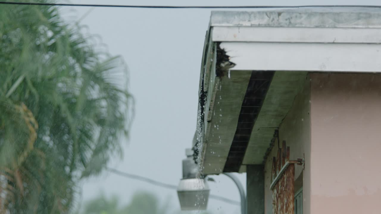 A house in the rain as water droplets form and fall off of the corner of the shed roof
