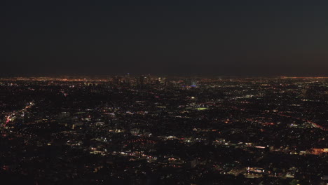 AERIAL:-Slow-flight-over-Hollywood-Hills-at-Night-with-view-on-Downtown-Los-Angeles-Skyline