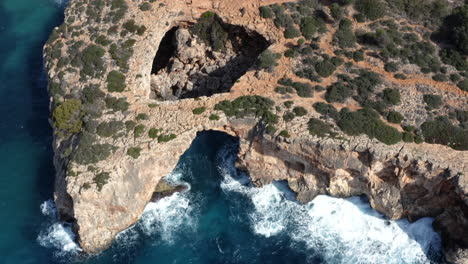 eroded rock cliffs of cala varques with arches above foamy sea waves