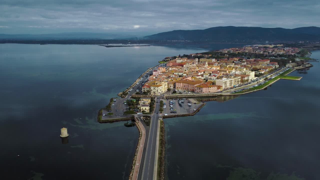 Traffico di auto su una strada-ponte attraverso la laguna verso l'antica città-isola di Orbetello, vicino al Monte Argentario e al Parco Naturale della Maremma in Toscana, Italia, con riflessi sull'acqua