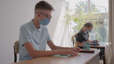 at school in the classroom children write in notebooks in protective masks observing a social distance. school education during the pandemic