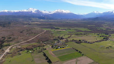 aerial shot of small houses in the middle of the immense mountain valley in trevelin, patagonia argentina. tulip fields, some pine trees and the snow capped andes in the background.