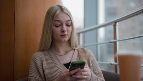 lady seated with phone in hand, looking thoughtful with blurred coffee on table and blurred city view outside the window, peaceful urban atmosphere, modern setting, quiet moment in cafe