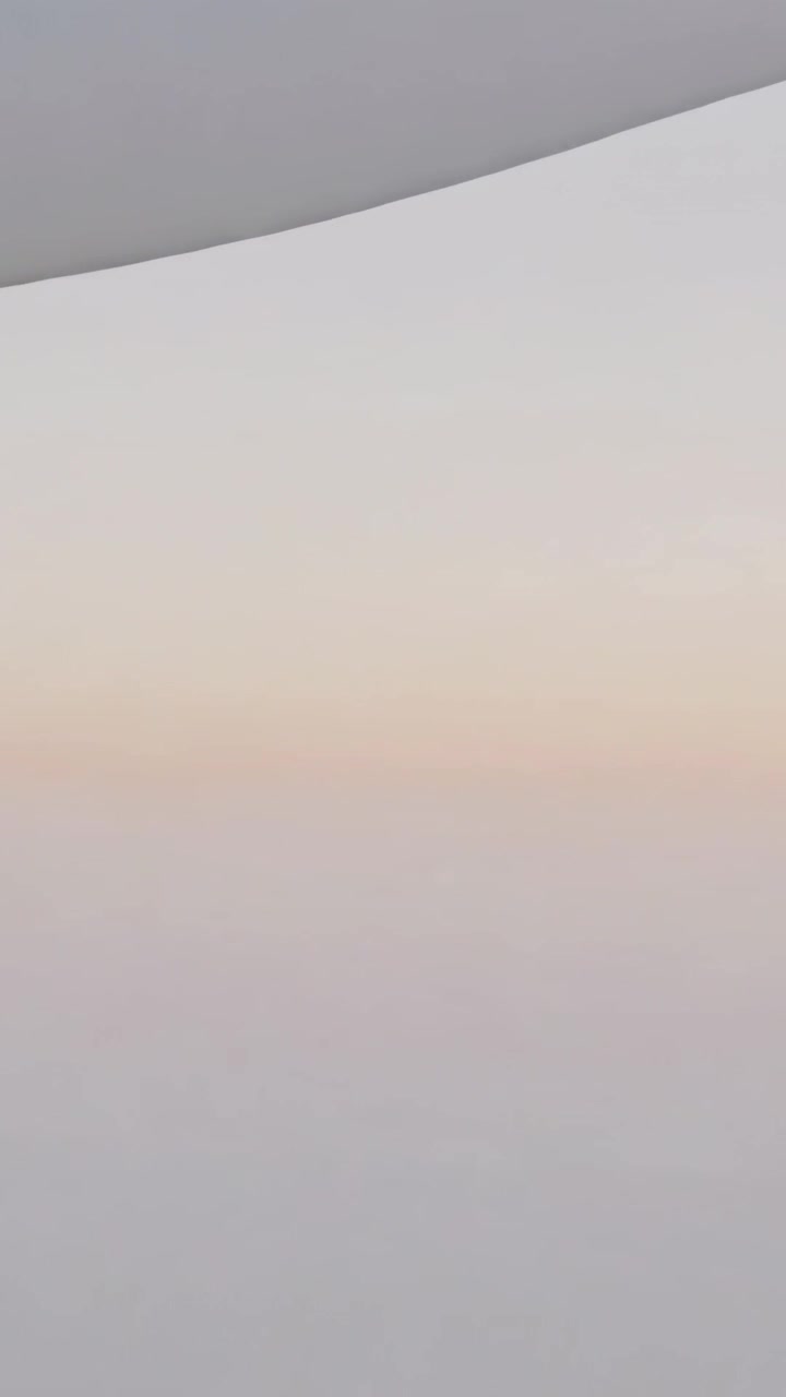 Video vertical: Cámara de aviación filmando la apertura de la persiana de una ventana, revelando un degradado de amanecer en capas.
