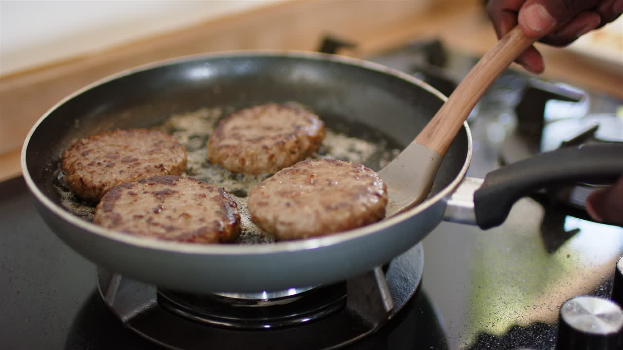 Cooking burgers in frying pan, person flipping patties on stovetop