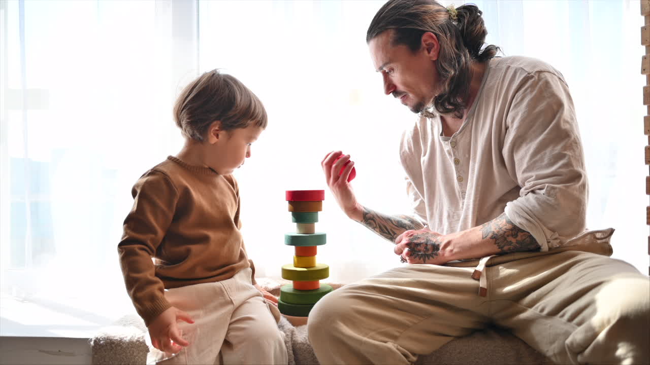 Father playing with his son with colourful, ecological wooden toys near a window