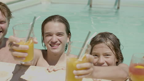 familia feliz en la piscina con sus cócteles junto a la piscina mirando a la cámara y sonriendo