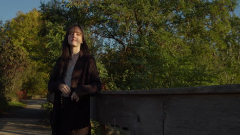a white, petite, slender girl leans against the railing of a bridge
