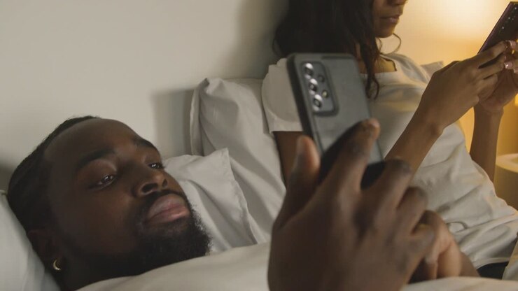Coppia con problemi di relazione a casa di notte a letto, entrambi che guardano i cellulari 3