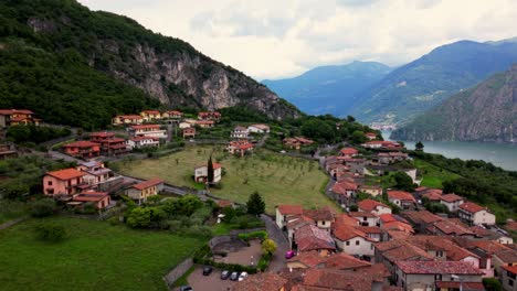 elevated orchard fields and colorful houses on steep terrain above lake iseo and alpine cliffs. shot at riva di solto, bergamo, italy