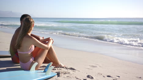 Una-Joven-Caucásica-Se-Sienta-En-Una-Tabla-De-Surf-En-La-Playa,-Sonriendo-Hacia-La-Cámara-Con-Espacio-Para-Copiar