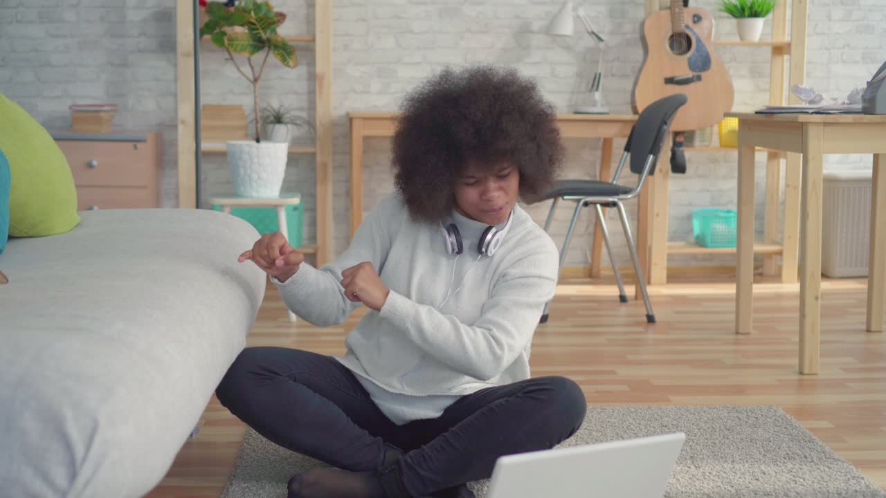 hermosa y alegre mujer afroamericana con un peinado afro sentada en el suelo con una computadora portátil aprendió sobre la victoria
