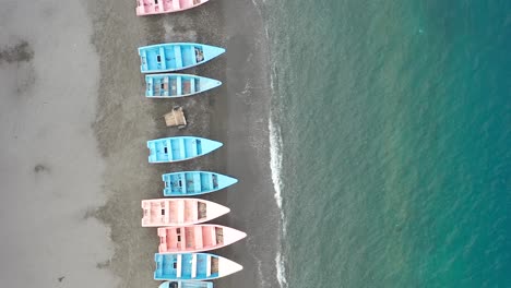 Aerial-drone-forward-view-along-Palmar-de-Ocoa-beach-with-colorful-pink-and-blue-small-boats-on-sea-shore