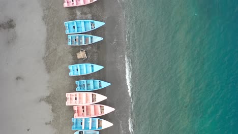 aerial drone forward view along palmar de ocoa beach with colorful pink and blue small boats on sea shore