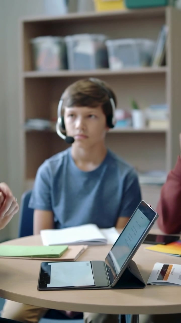 Video verticale: Ragazzo adolescente con cuffie che ascolta e segue un tutor che parla in una piccola classe con un tablet