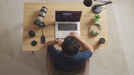 top view of a male color grading talking on smartphone while sitting in the workspace using a laptop next to the camera editing the video at home