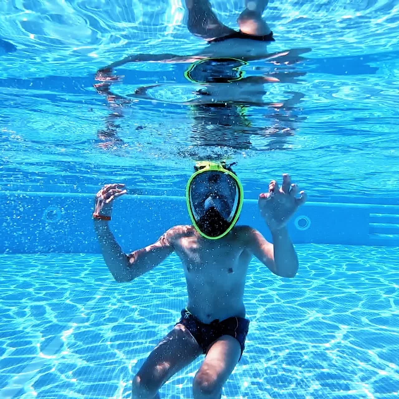 Teenage boy having fun inside the swimming pool. Boy in mask enjoys underwater in the pool. Happy summer vacation.
