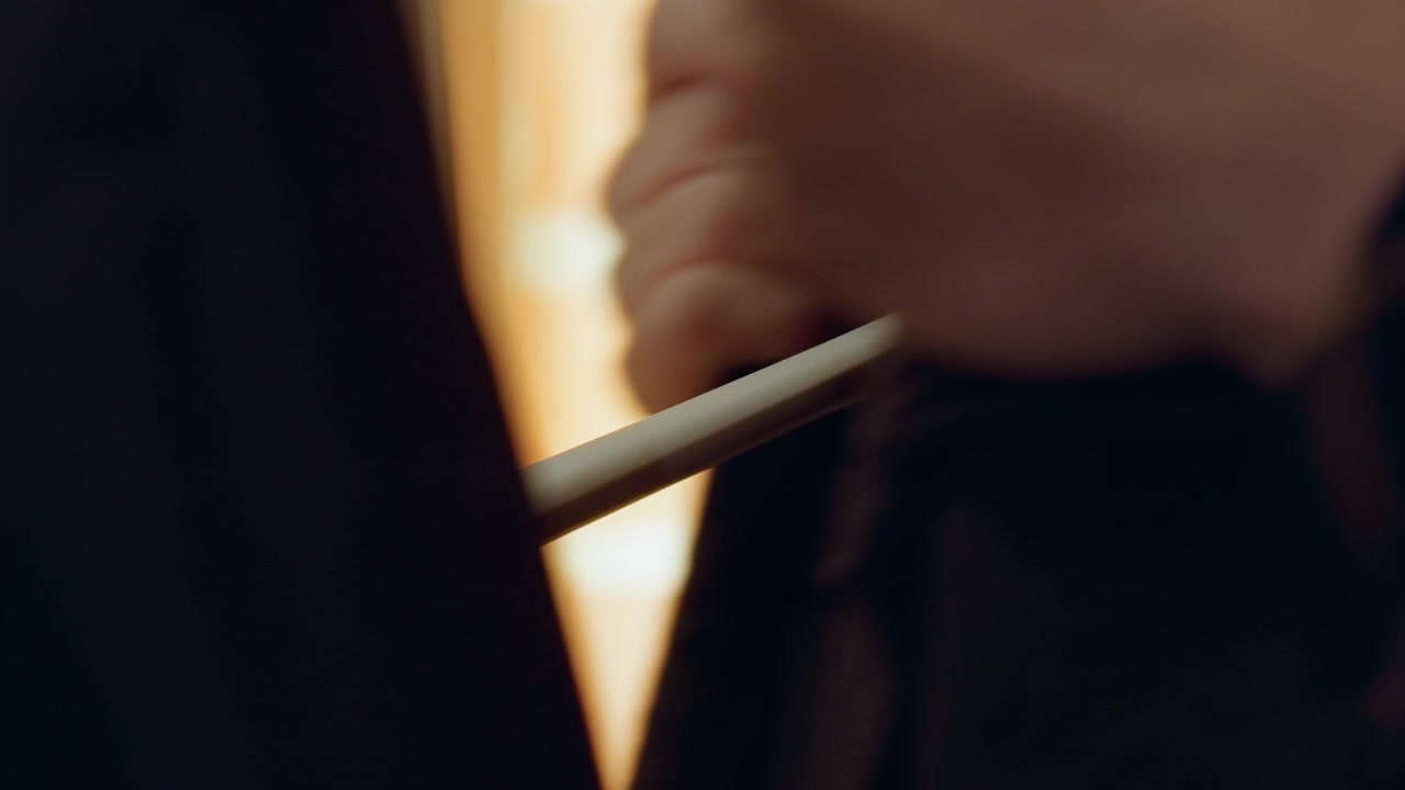 Close up of hand holding and adjusting dark fabric revealing texture details against warm toned background. Hand movements focus on garment manipulation with soft lighting highlighting