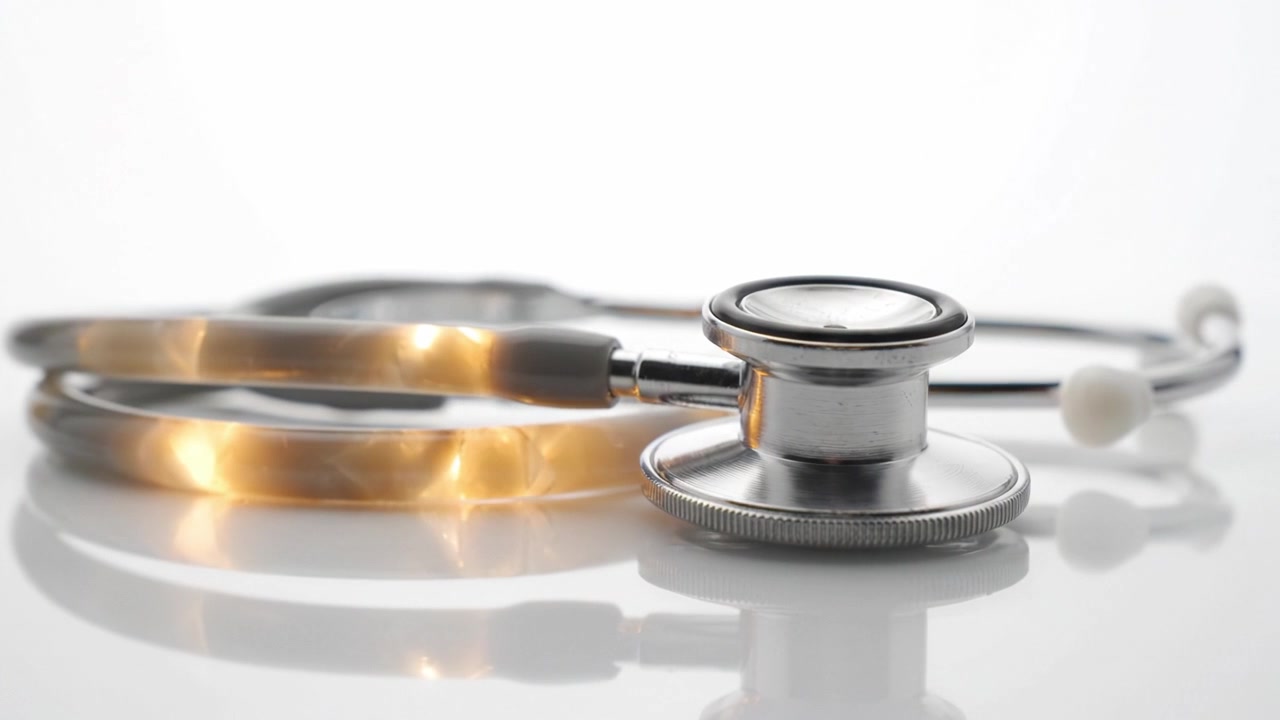 Close-up of a stethoscope on a reflective surface, highlighting the shiny metal components and the flexible tubing, emphasizing medical examination tools.