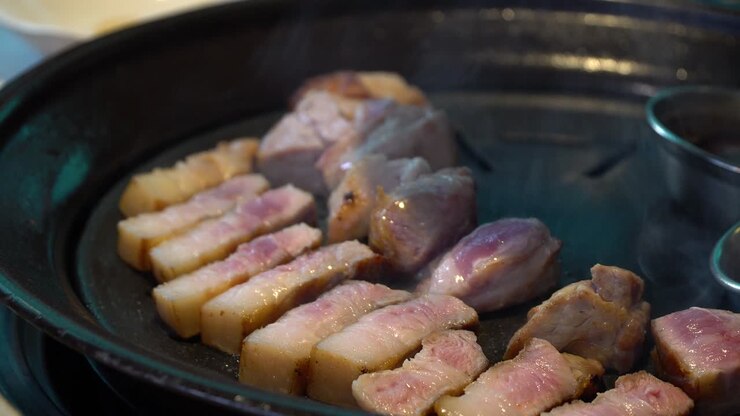 Un uomo cucina pancetta di maiale coreana in una griglia di ferro calda - primo piano.