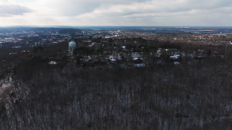 Mount-sequoyah-over-bare-winter-trees,-with-a-water-tower-and-town-in-distance,-late-afternoon,-aerial-view