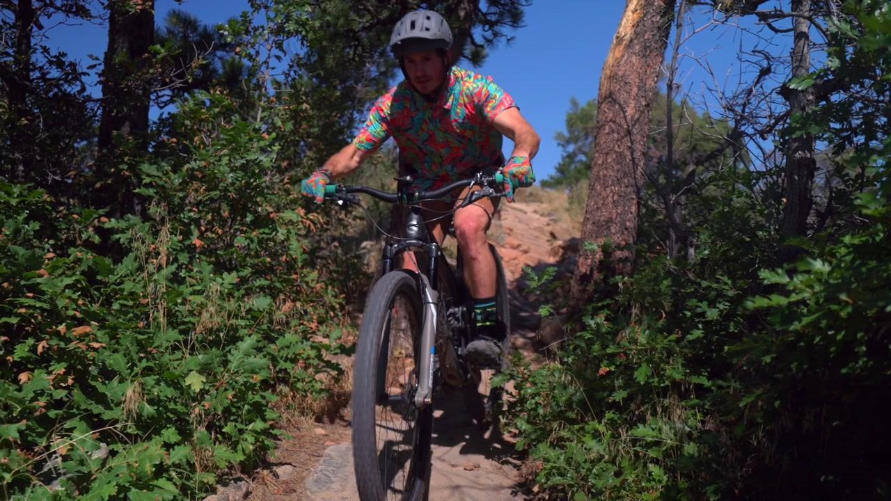 Ciclista adulto de mountain bike descendo em Red Rocks, Morrison, Golden, Colorado, passando por fendas de pedras e árvores, com acompanhamento panorâmico. Nas trilhas Dinosaur Ridge e Dakota Ridge, praticando esporte e fitness nos sopés de Denver, Front Range, em um dia ensolarado.