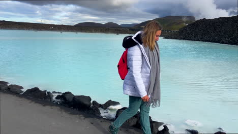 Schönes-Blondes-Mädchen,-Das-Am-Türkisfarbenen-Wasser-Der-Blauen-Lagune-In-Island-Spaziert