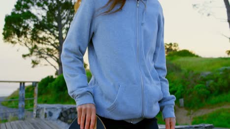 front view of young caucasian female skateboarder walking with skateboard at observation point 4k