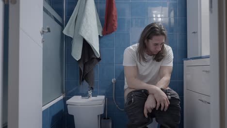 man sitting on toilet in bathroom