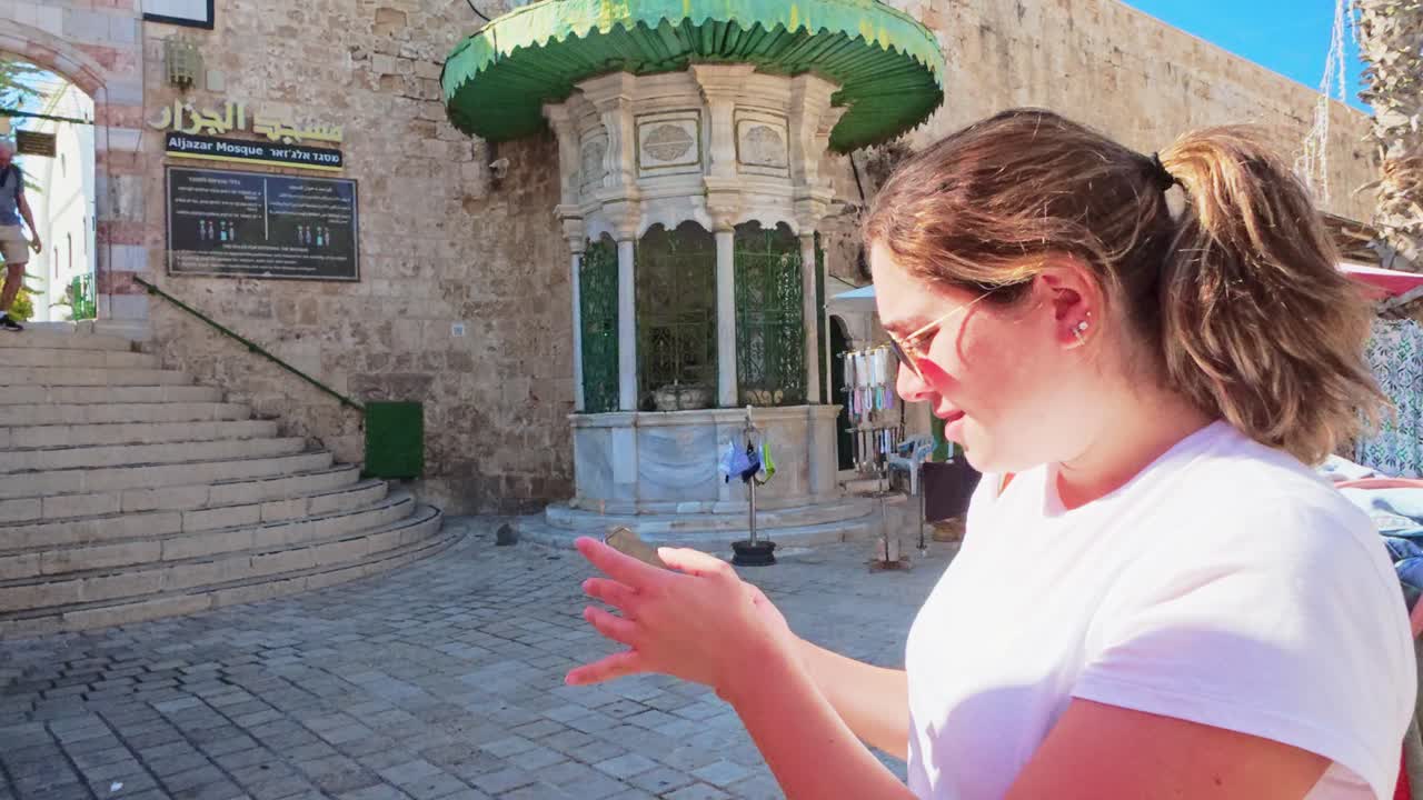 Giovane donna che guarda lo schermo di uno smartphone mentre si trova in una piazza di pietra