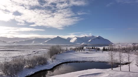 Aerial view showcases the dramatic winter landscape of Borgarfjörður, Iceland, featuring tranquil fjord waters reflecting cloudy skies and snow-capped mountains, including Hafnarfjall, Kessuhorn