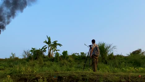 a documentary filmmaker, photographer is working on a pollution site and shooting a petroleum refinery gas flare blazing fire pouring thick black smoke