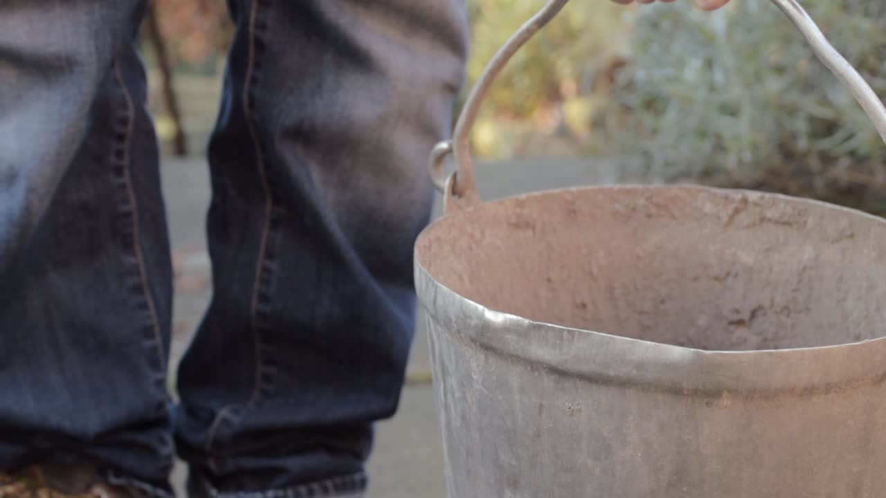 Lady putting metal bucket on garden pathway close up