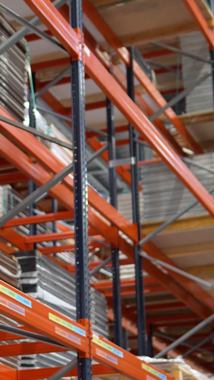 Primo piano di scaffalature metalliche arancioni in un grande centro di distribuzione che contengono materiali in legno impilati per l'industria del mobile.