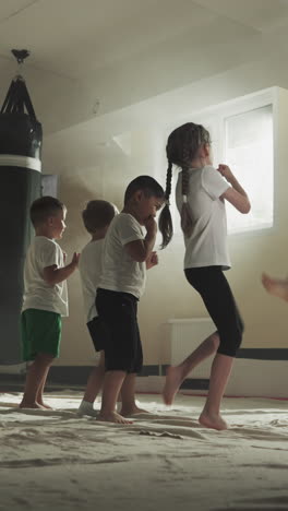 los niños hacen patadas con el instructor en la escuela de karate. los niños pequeños entrenan técnicas de lucha con las piernas con el joven entrenador en el gimnasio en cámara lenta. artes marciales