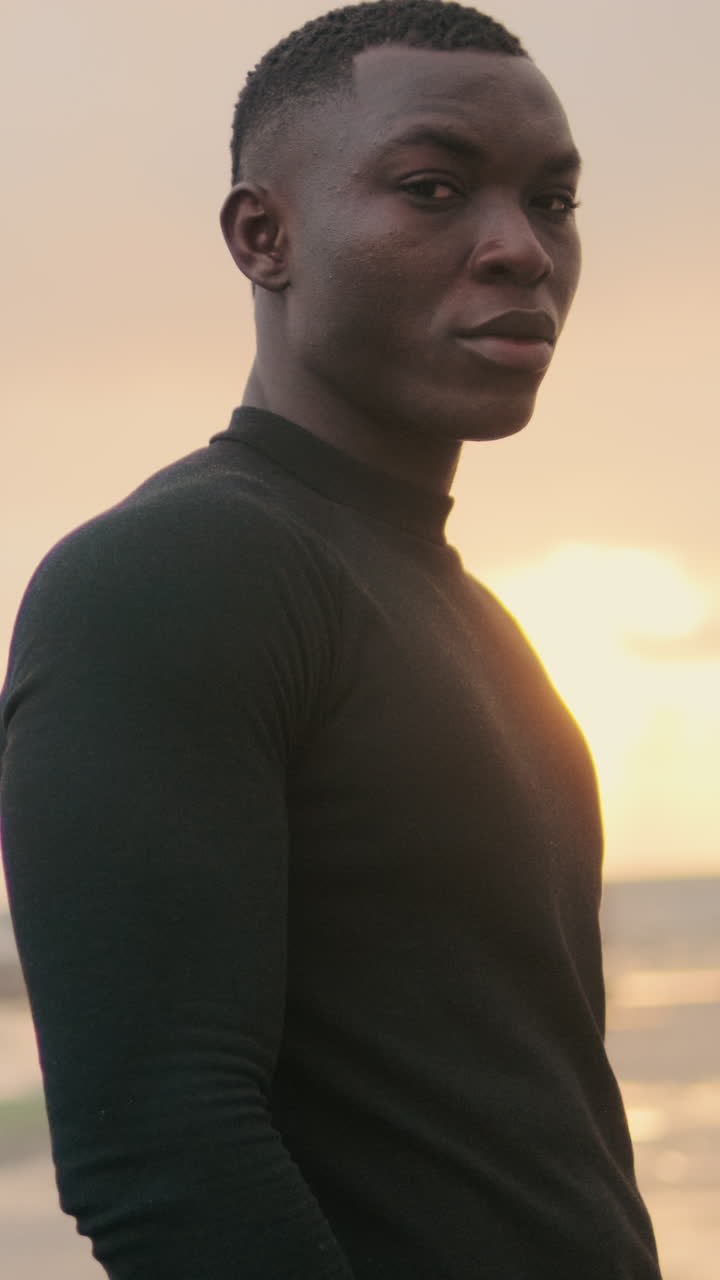 Joven afroamericano de pie pensativo al atardecer junto al océano
