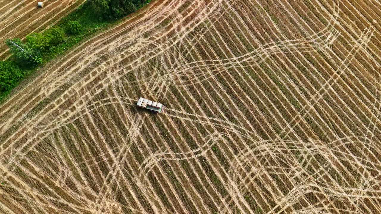Tractor trailer with bales on Baled hay fields in agricultural landscape with tire marks