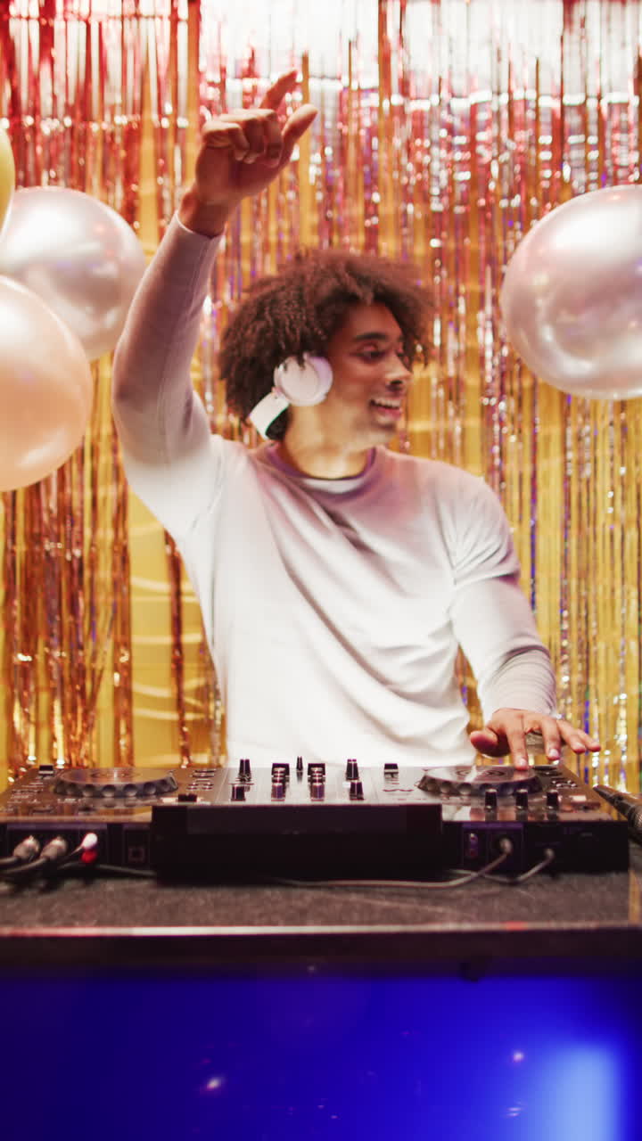 Vertical video of happy african american male dj playing music and dancing at a nightclub