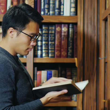 Gut-Aussehender-Asiatischer-Mann-Mit-Brille,-Der-Ein-Buch-In-Der-Bibliothek-Liest-2