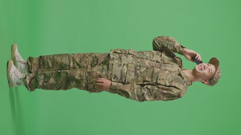 full body of side view asian man soldier talking on smartphone and looking around while standing in the green screen background studio
