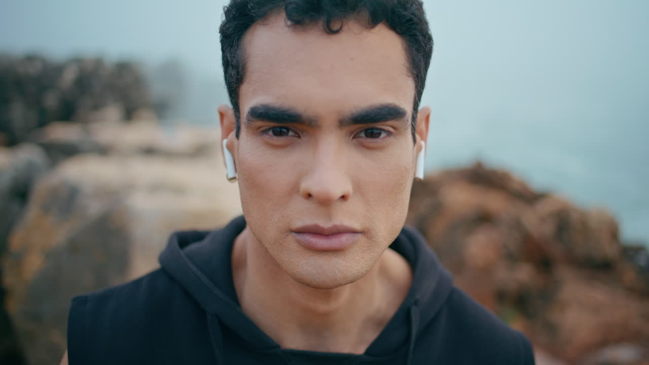 Ritratto di uomo bruno in posa su una scogliera con vista sull'oceano. Primo piano di un affascinante ragazzo atletico.
