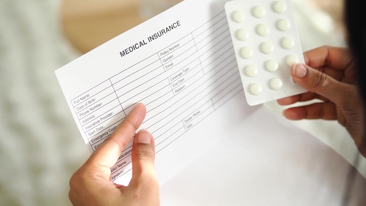 Hands Holding Medical Insurance Form and Blister Pack of Pills