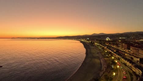 aerial view of nice, france coastline at dusk with city lights, mediterranean sea, and glowing orange sunset sky over the promenade des anglais